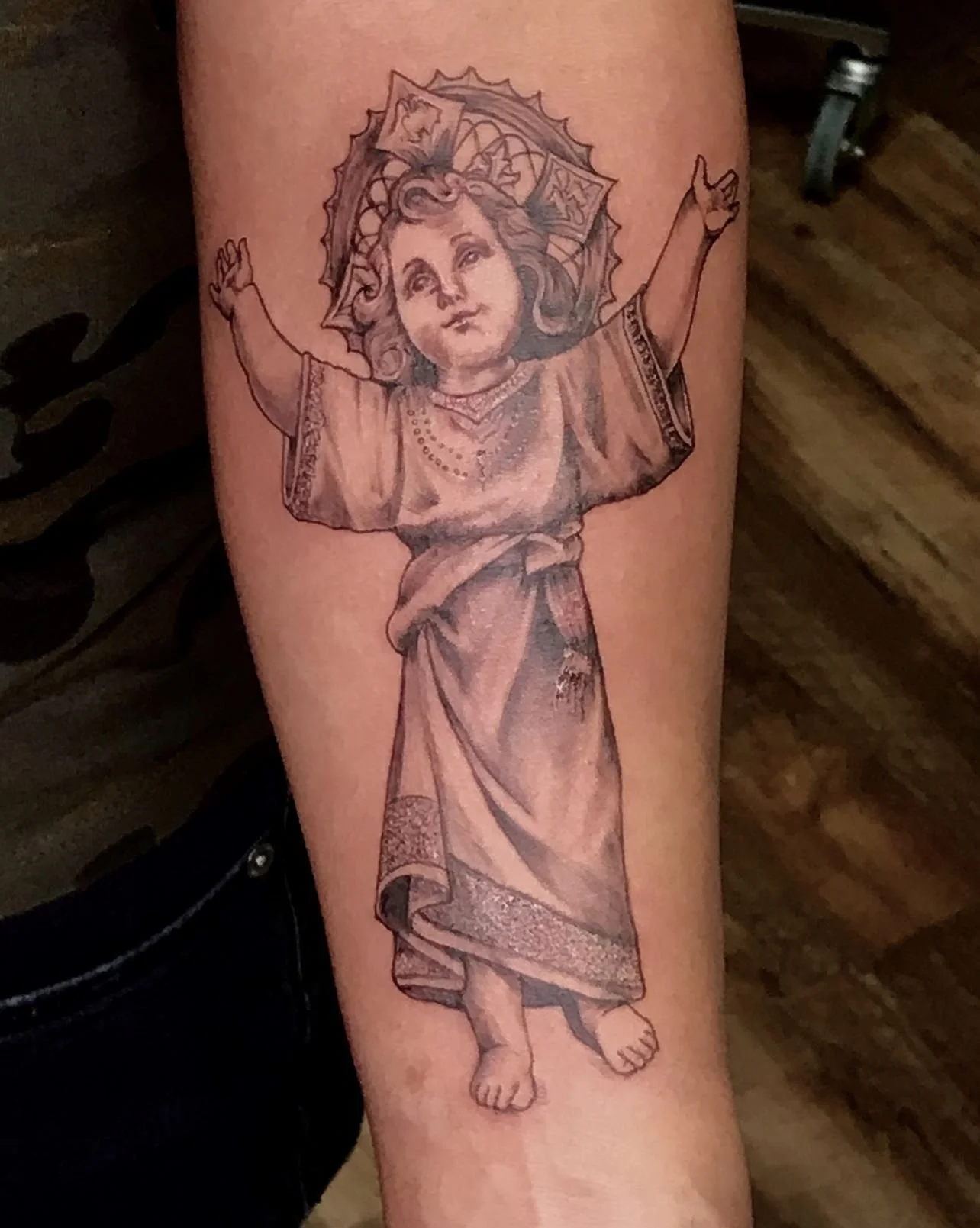 Black and grey realism tattoo of Infant Jesus with halo and raised arms, religious tattoo  created in Bronx NYC