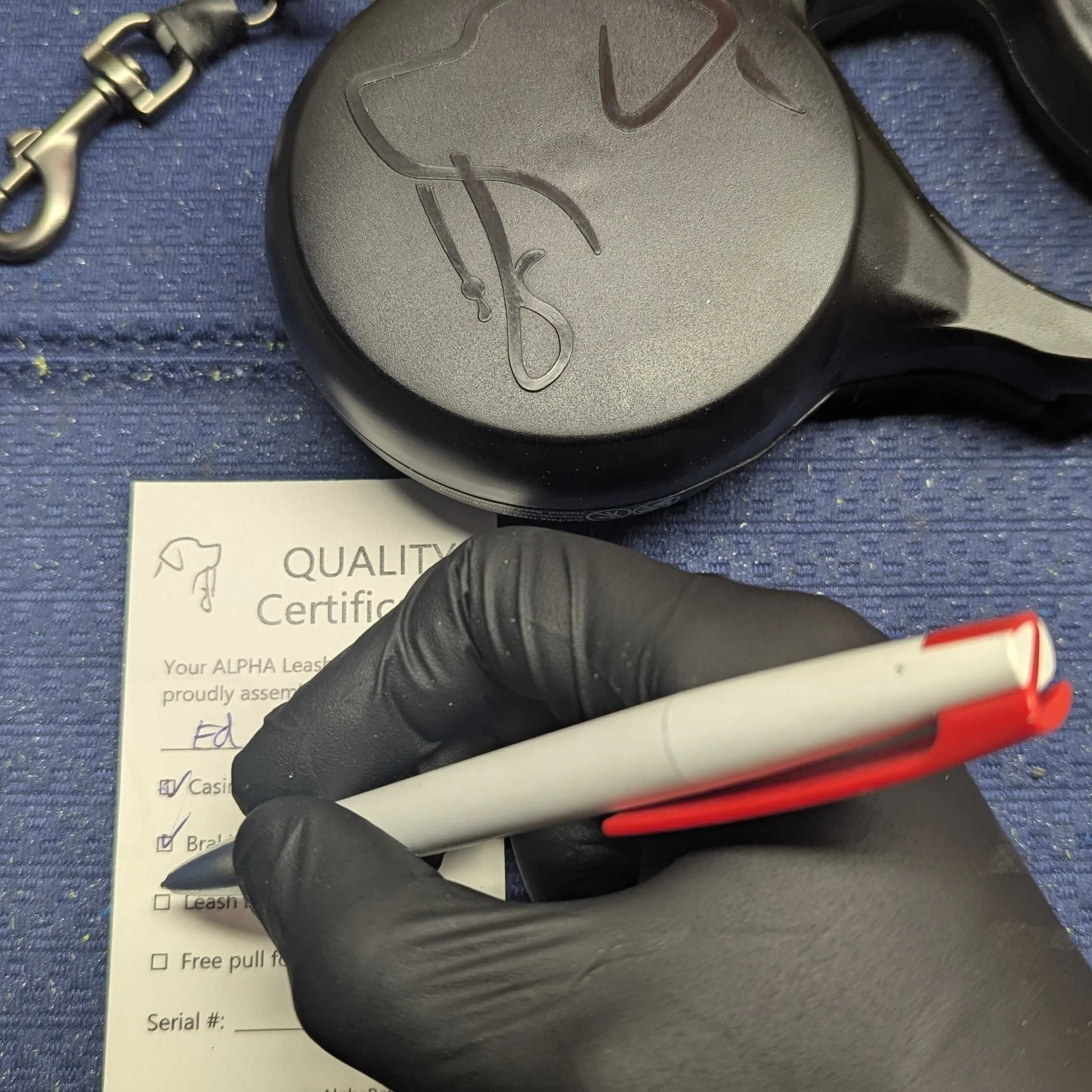 Close-up of a hand in a black latex glove filling out the quality check sheet for a new Alpha Leash.