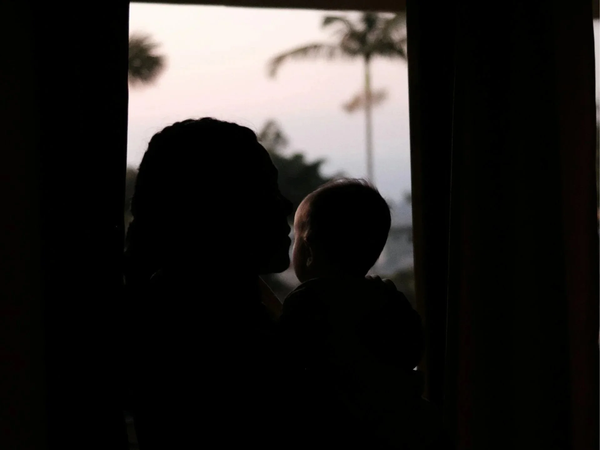 Mother and children seen from behind standing in a sunlit doorway