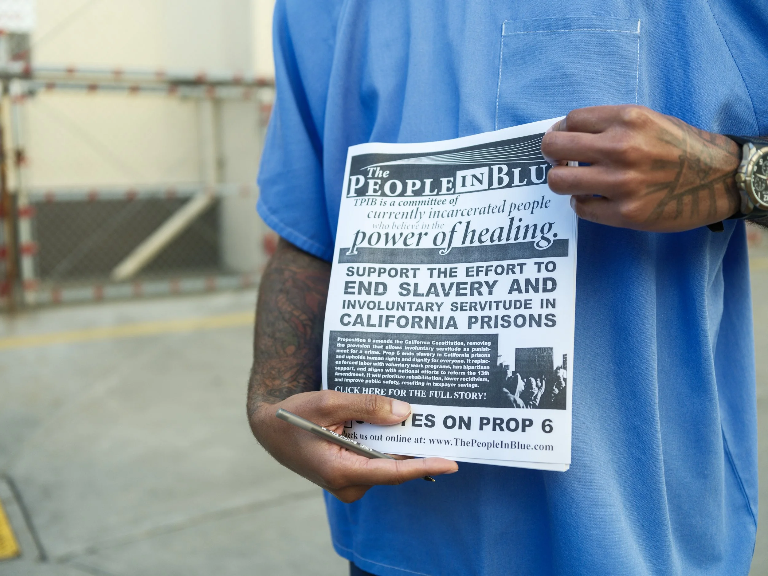 Person in a blue shirt holding a flyer regarding Proposition 6 and the effort to end slavery and involuntary servitude in California prisons.