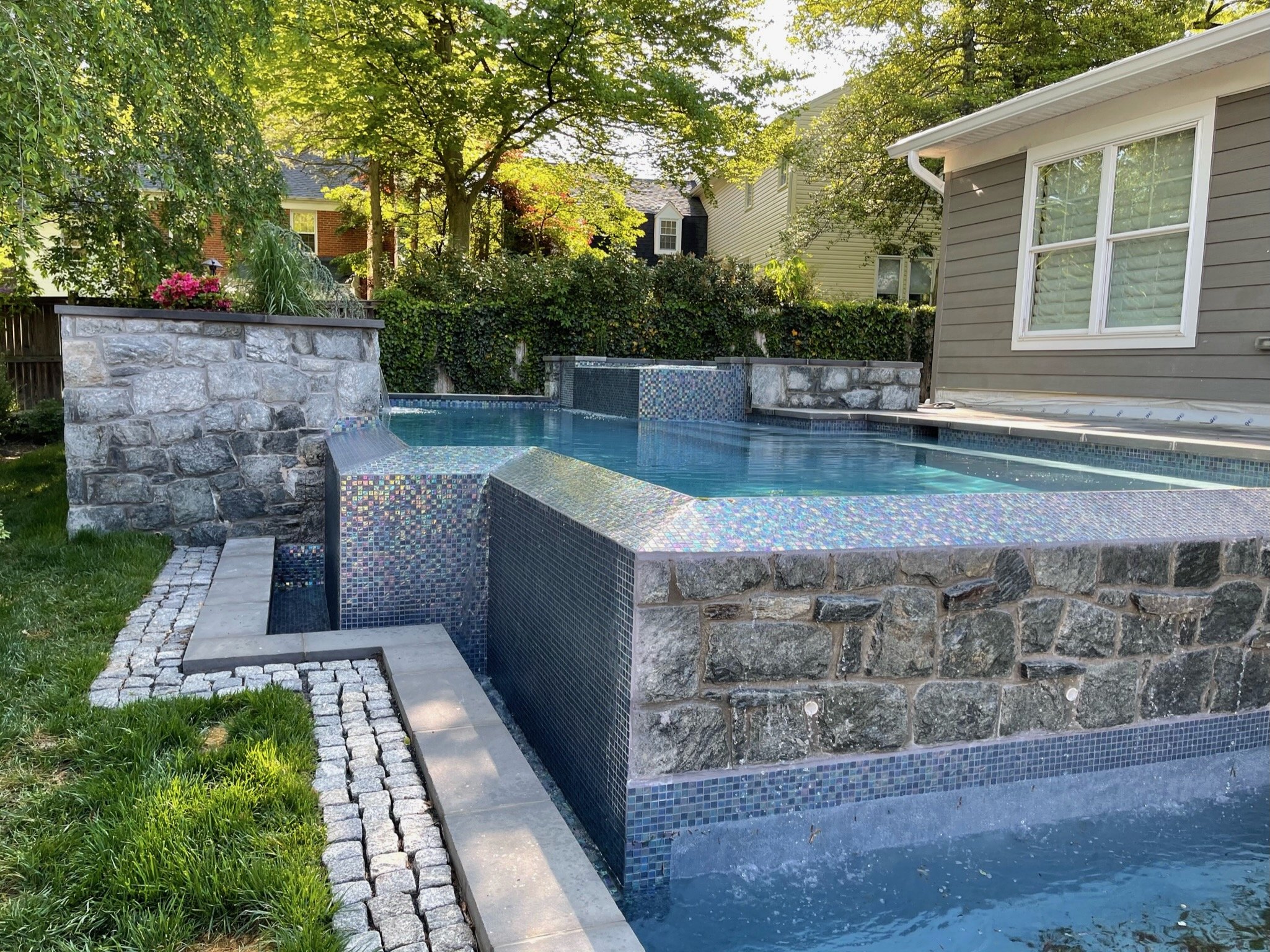 Raised pool with mosaic tile, natural stone walls and an overflow water feature.