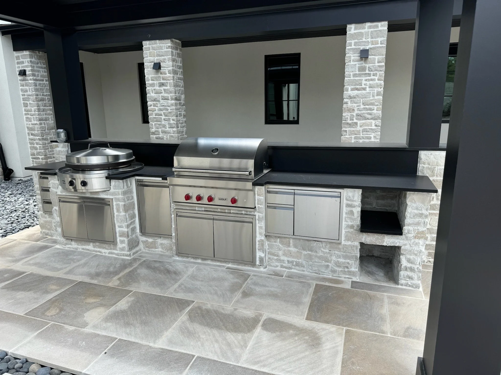 Built-in outdoor kitchen with stone masonry, stainless steel grills and a stone patio.