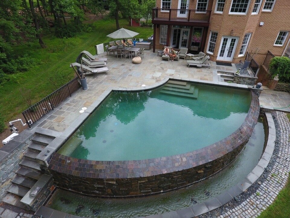 Curved infinity-edge pool with a stone terrace, steps and outdoor seating.