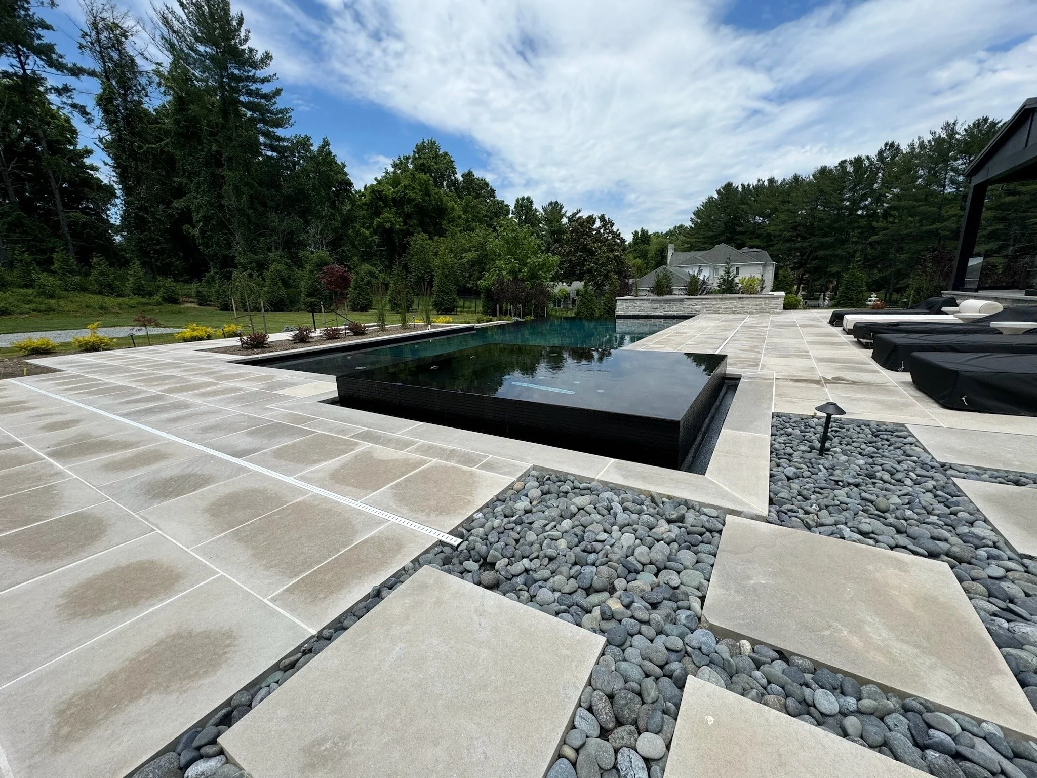 Outdoor living with a pool, spa, stone terrace and landscaped surroundings.