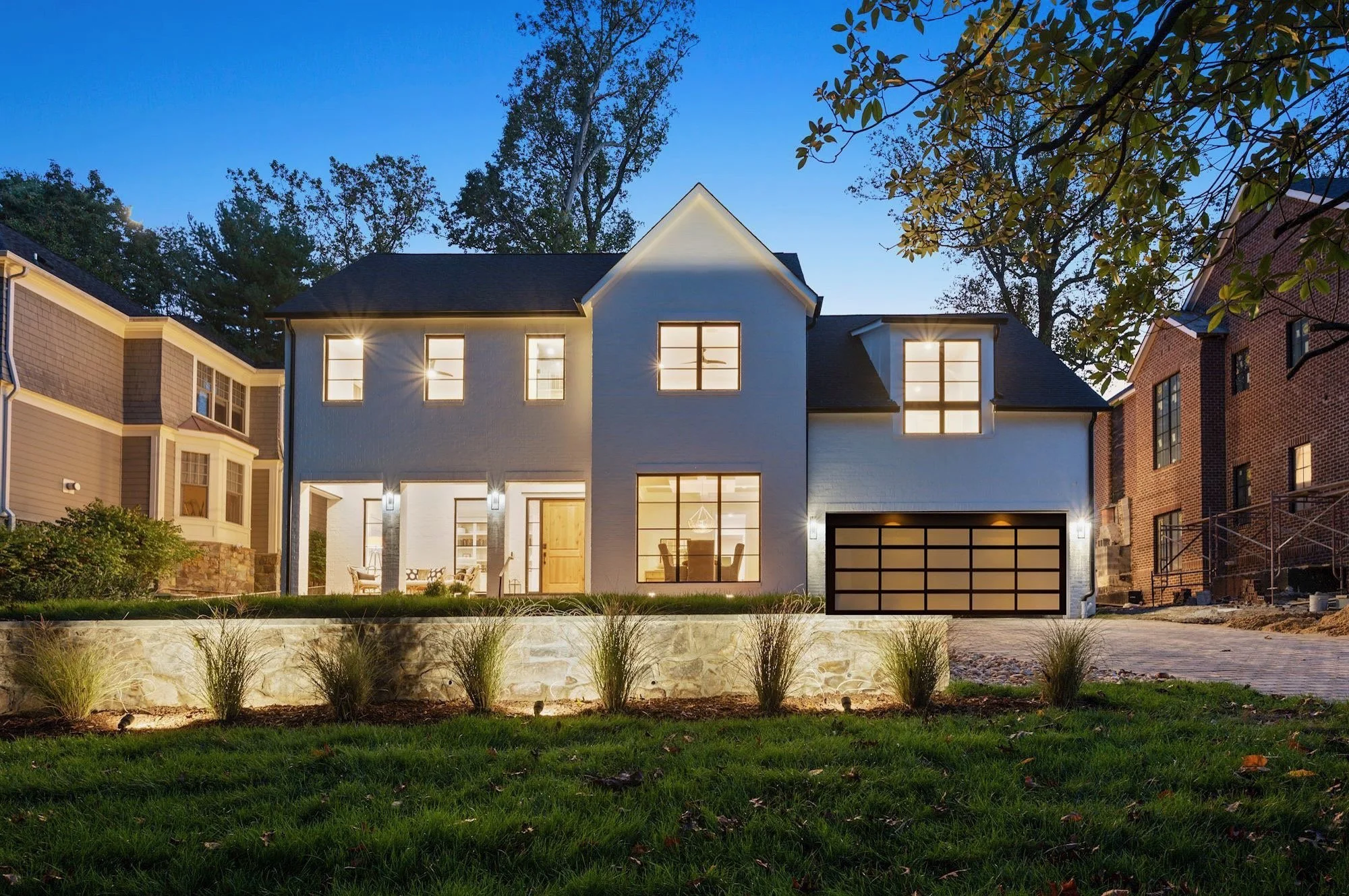 Completed custom home with illuminated windows and landscaped terraces at dusk.