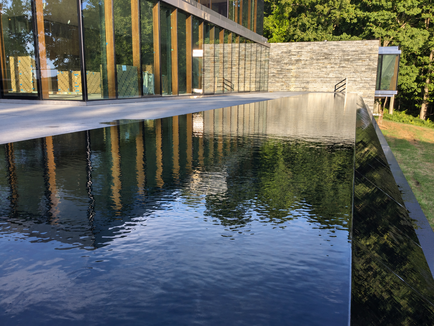 Modern infinity-edge pool beside a glass-fronted home and pale stone terrace.