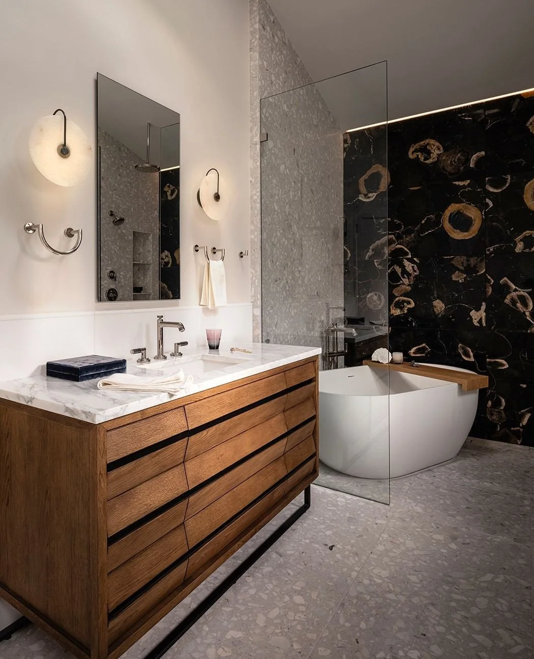Escape to serenity. Petrified wood and terrazzo stone create a soothing ambiance in this bathroom sanctuary. @kallista vanity and fixtures provide sleek sophistication, while @alliedmaker sconces illuminate the space with warmth. 
📸@_karamercer 
#re