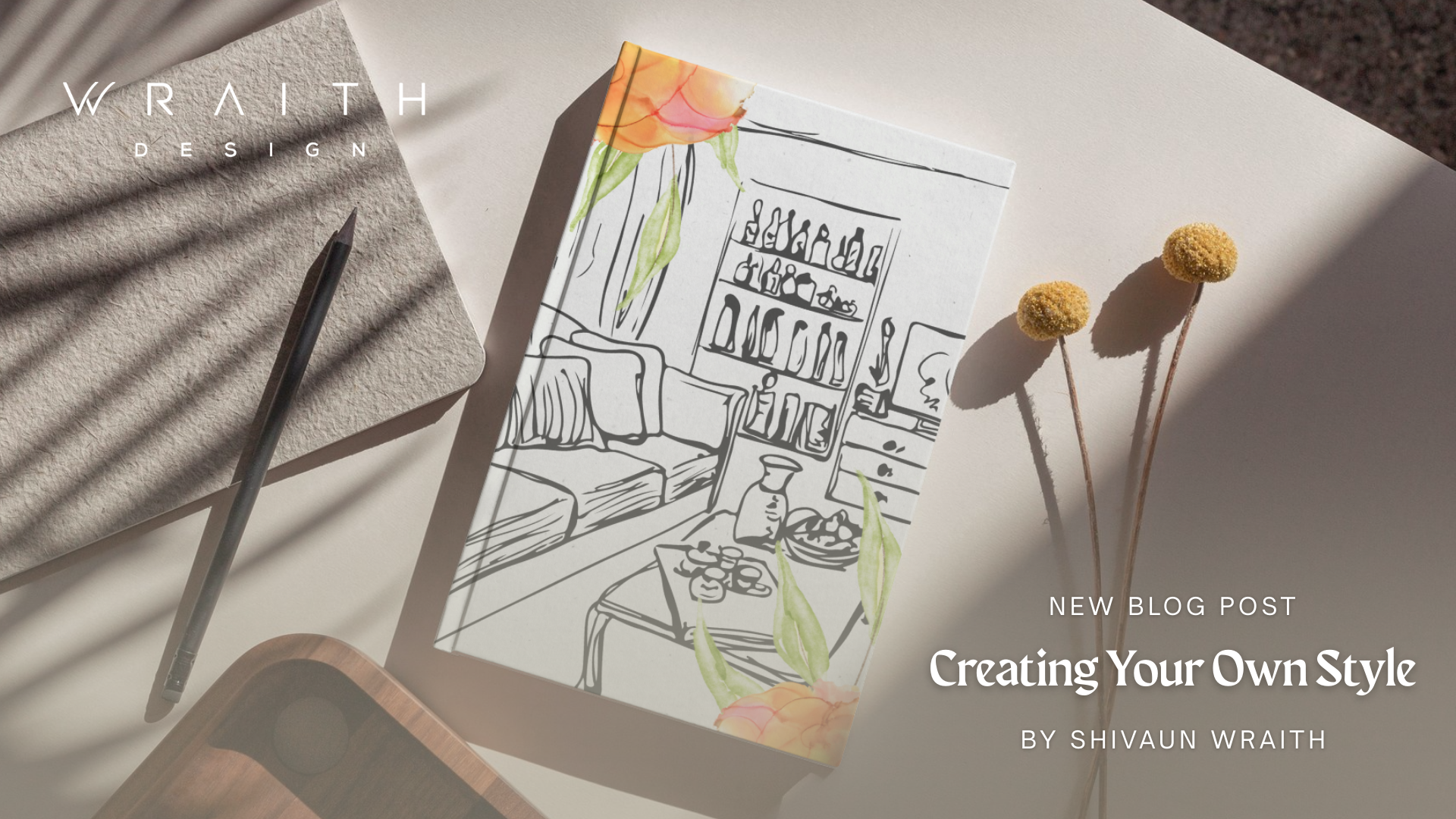 A desk scene with a pen, a textured gray notebook, and a rectangular card featuring a black and white line drawing of a living room interior, decorated with a floral border. Two yellow billy buttons are also on the desk, casting shadows.