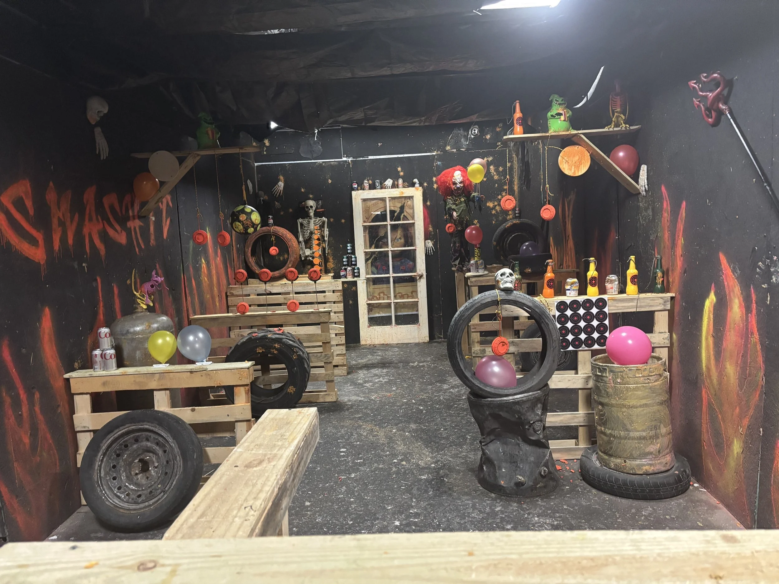A decorated game room with pirate theme, featuring balloons, skulls, tires, wooden pallets, and painted flames on the walls.