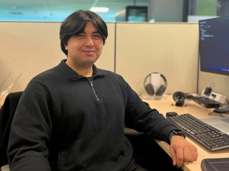 Mark De Guzman, PUMA full stack developer intern, sits at his desk next to a computer