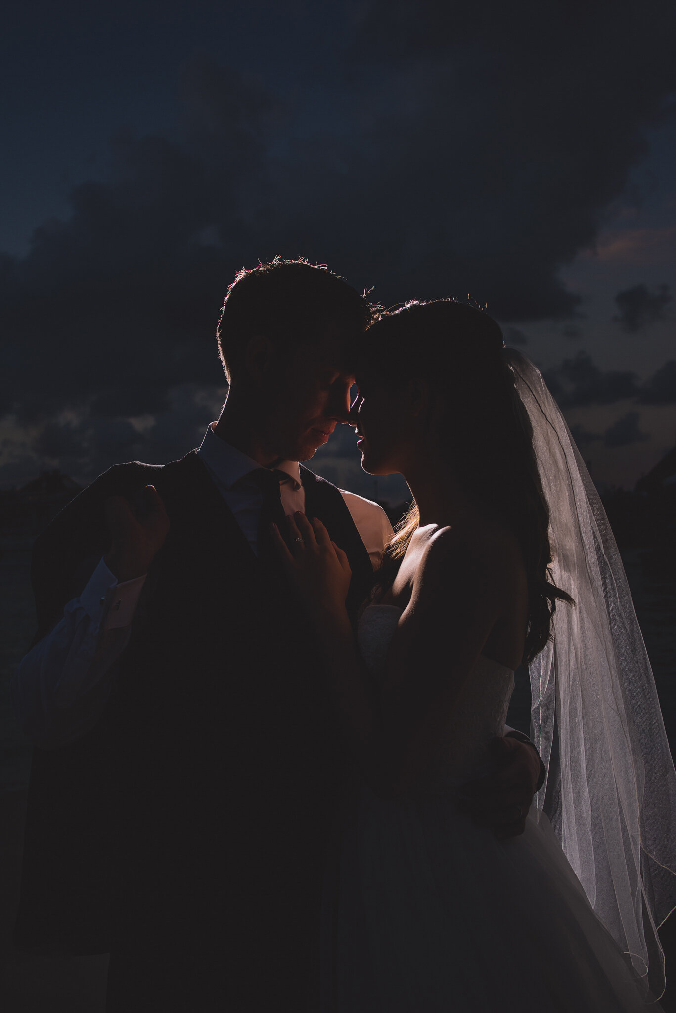 bride and groom headbump backlit in dramatic lighting dark and moody