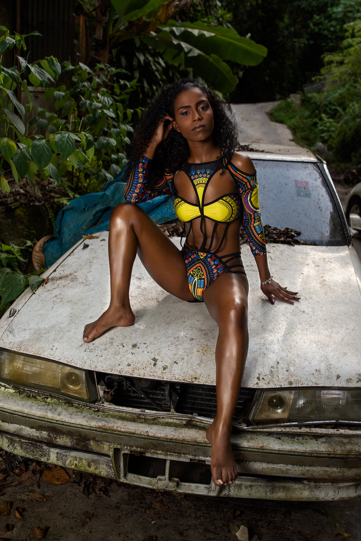 model in bikini sitting on old white car in fern gully