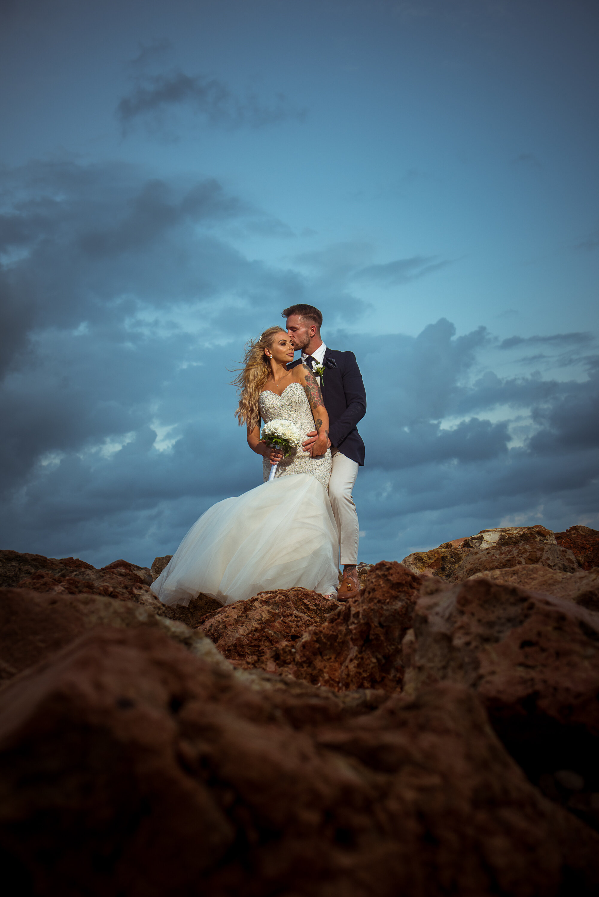 bride and groom standing on rocks with dark moody dramatic sky, royalton white sands