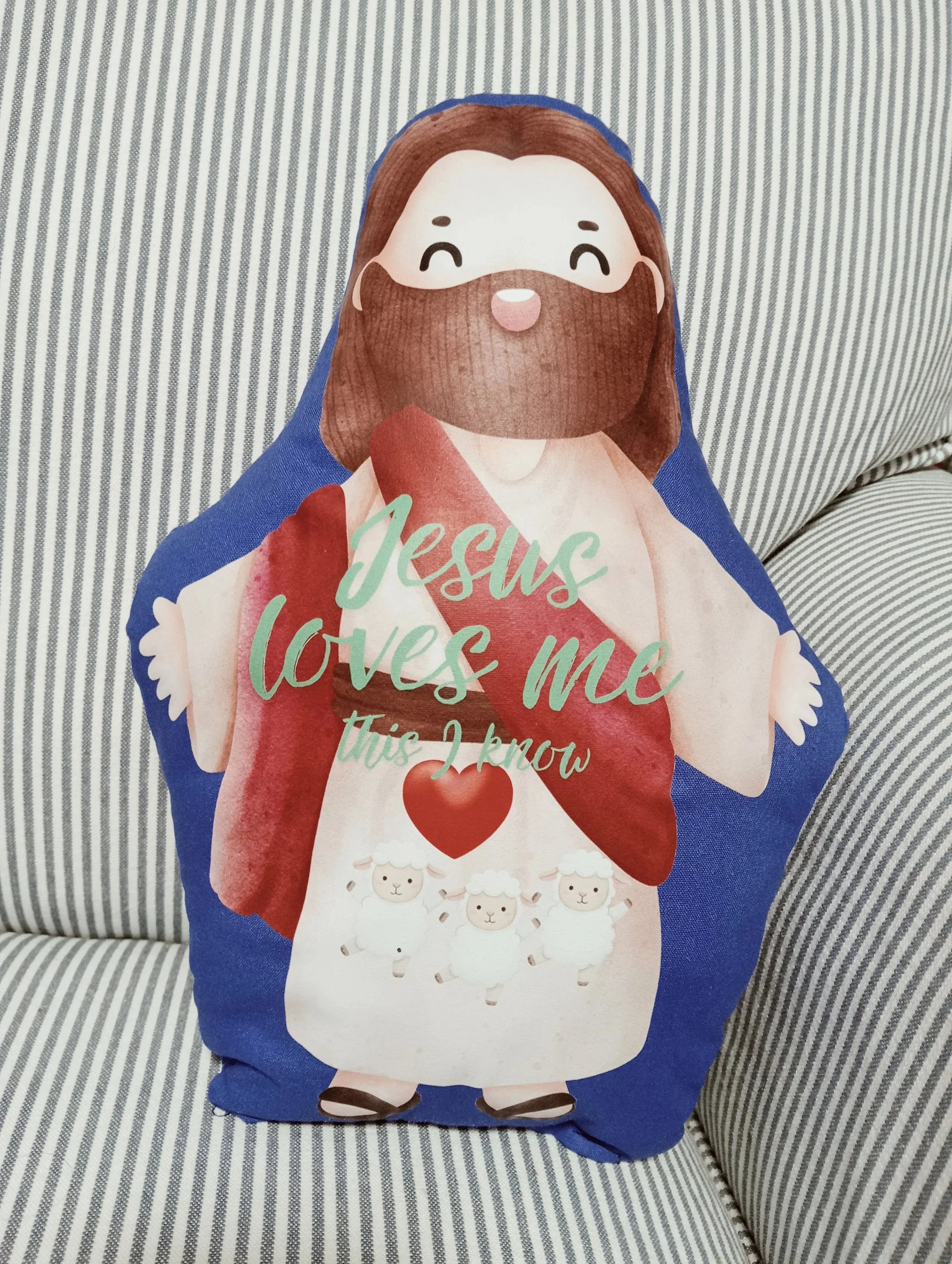 An adorable adaption of Jesus in the form of a huggable cushion. Comes with the phrase ‘Jesus loves Me This I know’ and three baby lamb’s on His lap.