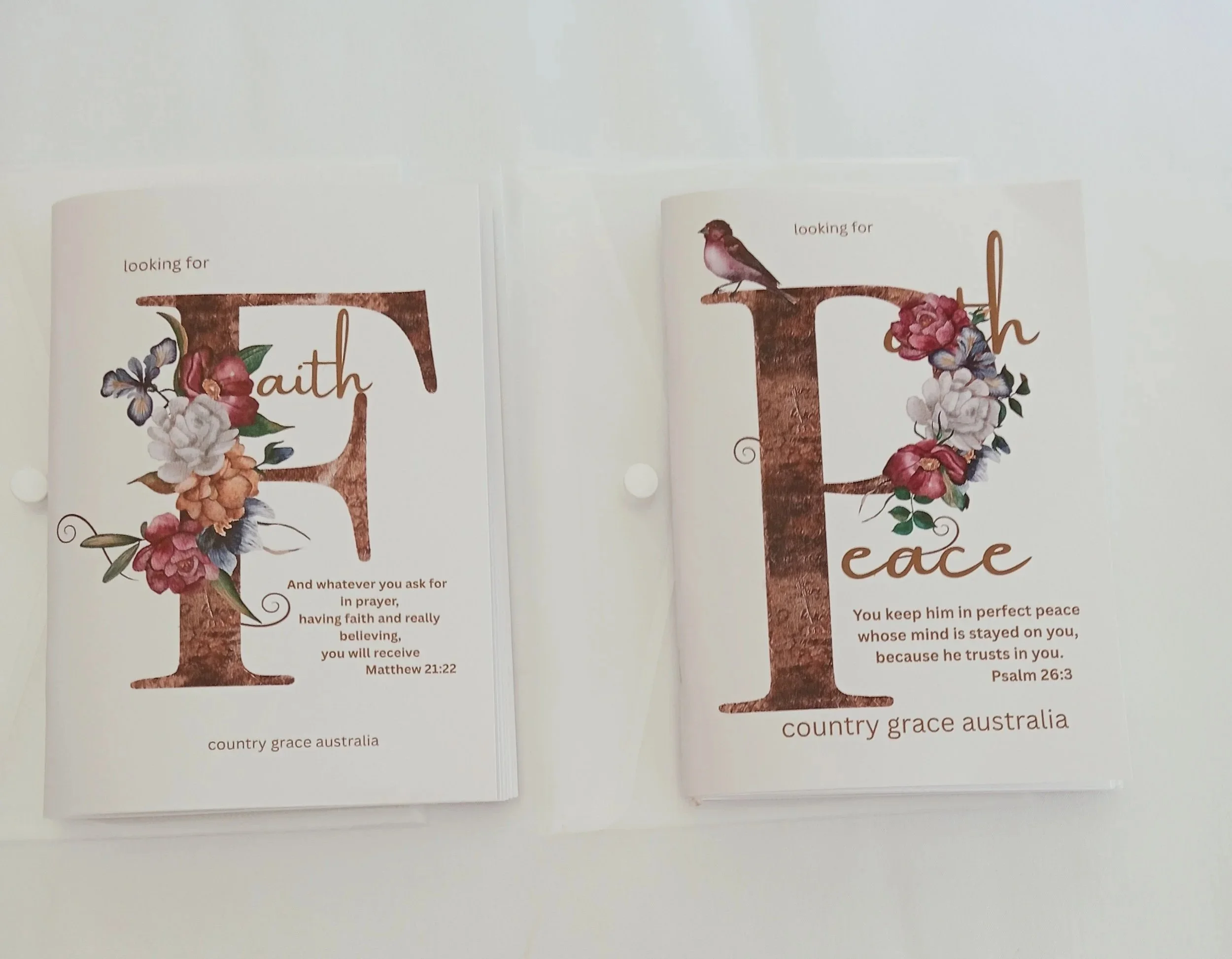 Two printed cards with floral designs and the words "Faith" and "Peace". The card on the left features a floral arrangement and a Bible verse from Matthew 21:22. The card on the right features a bird sitting on the top of the letter "L" with a floral arrangement and a Bible verse from Psalm 26:3.