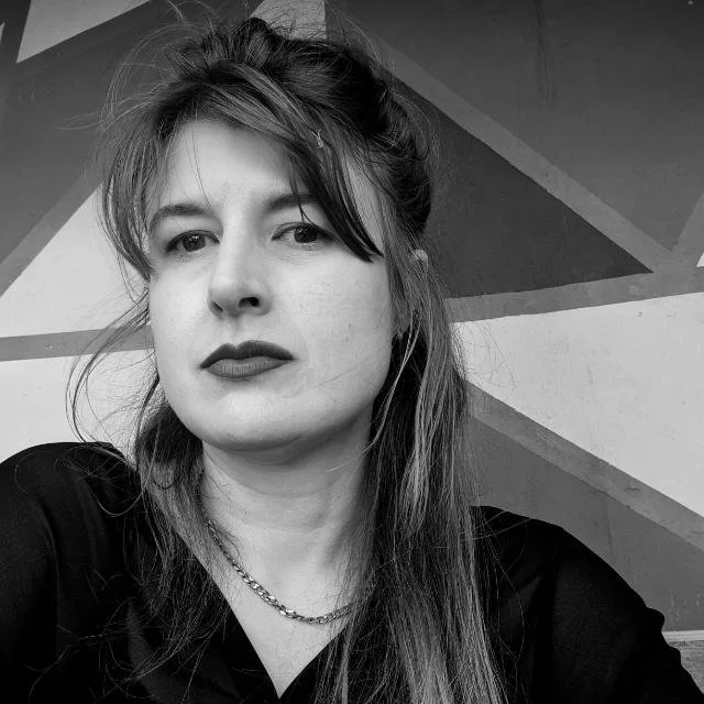 Black and white photo of a Claire Carroll with long hair and lipstick, posing against an abstract geometric background.