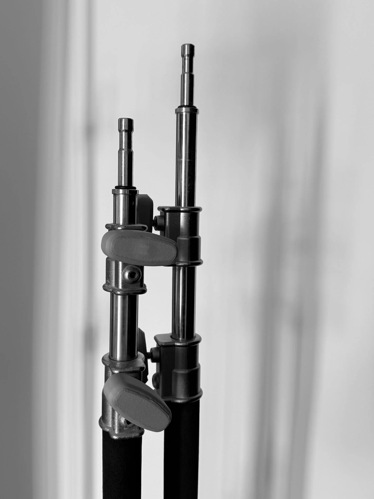 Close-up of two metal telescopic rods with adjustable clamps, set against a plain background.