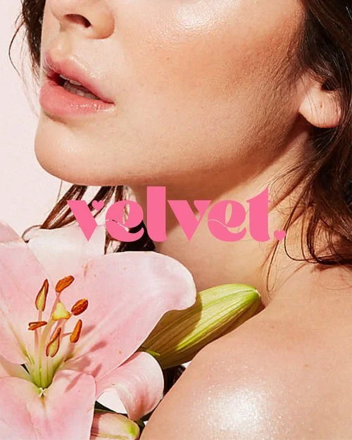 Close-up of a woman's face and shoulder with pink lily flower, pink text reading 'velvety.'