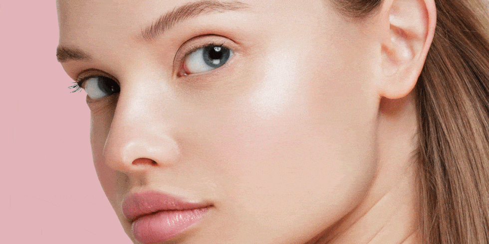 Close-up of a woman's face with clear skin, blue eyes, pink lips, and light makeup against a pink background.
