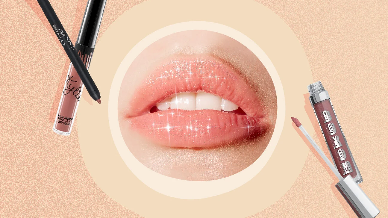 Close-up of glossy, sparkly lips and makeup lip gloss and liquid lipstick tubes with applicators on a peach-colored background.