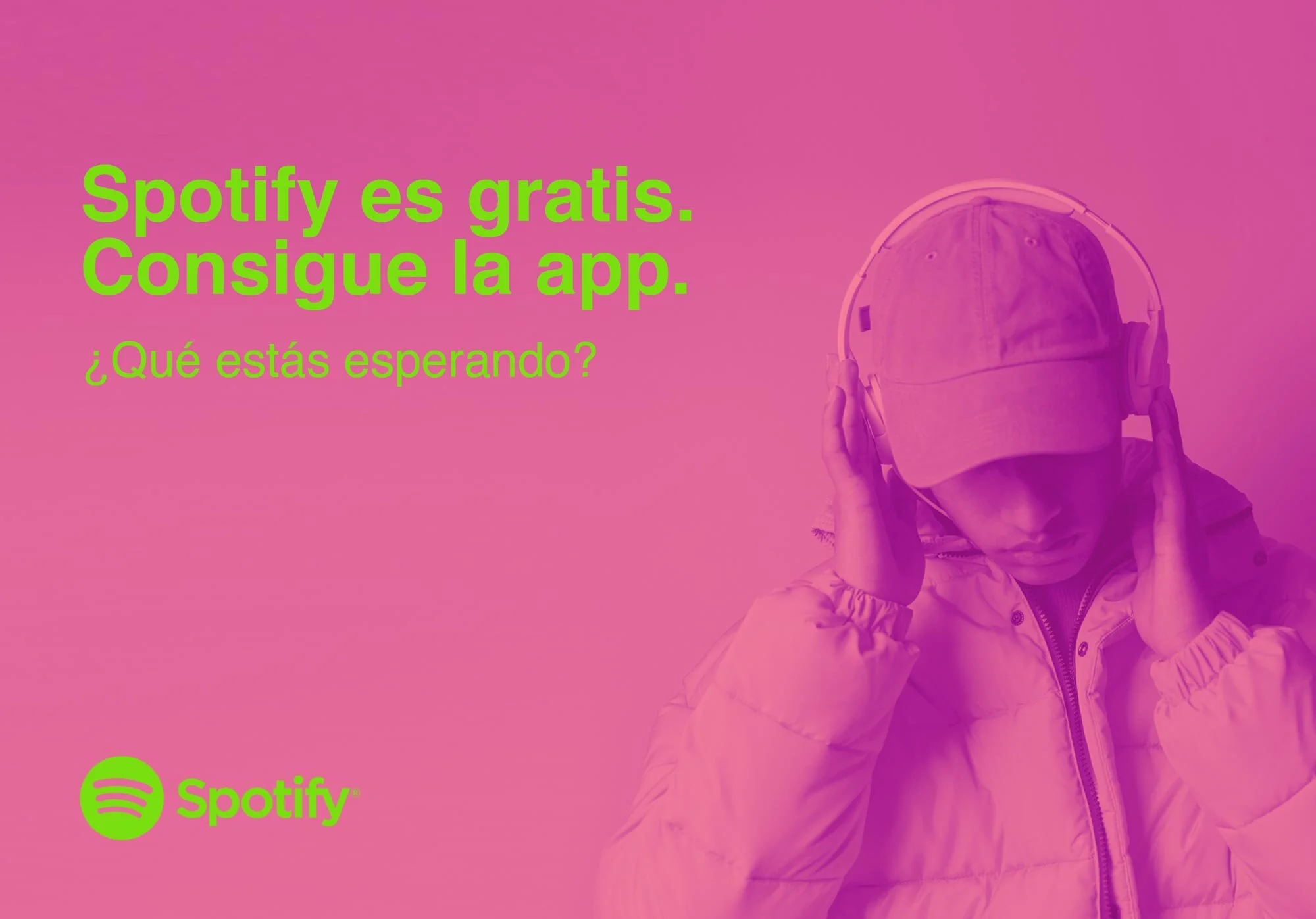 A person wearing a beige baseball cap and jacket holds a pair of large gray headphones to their ears against a pink background with green text promoting Spotify in Spanish.