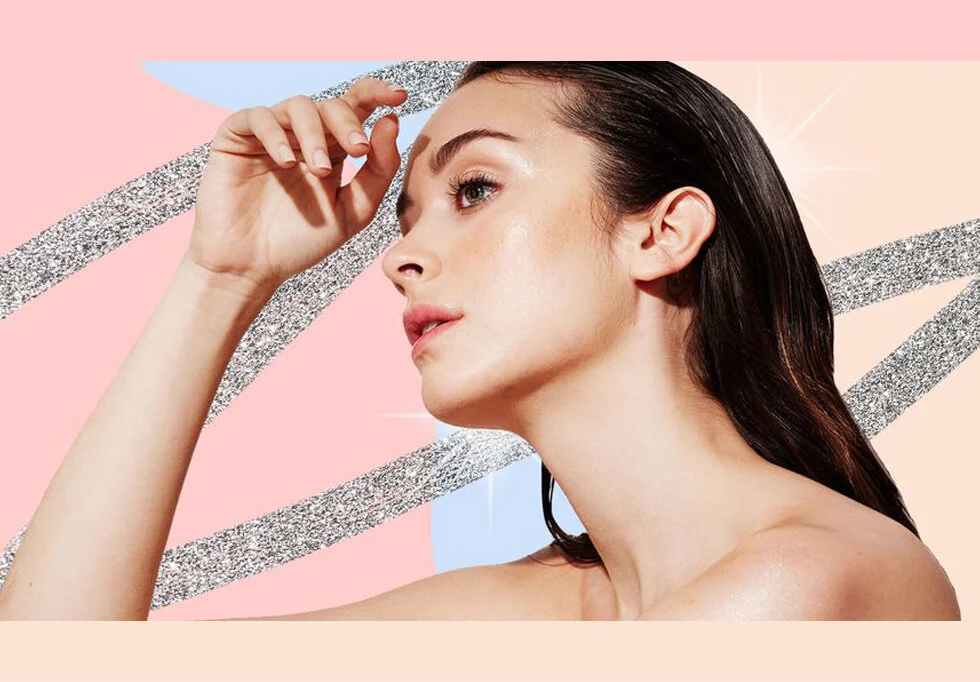 A young woman with black hair and clear skin is posing with her right hand touching her forehead against a colorful abstract background.