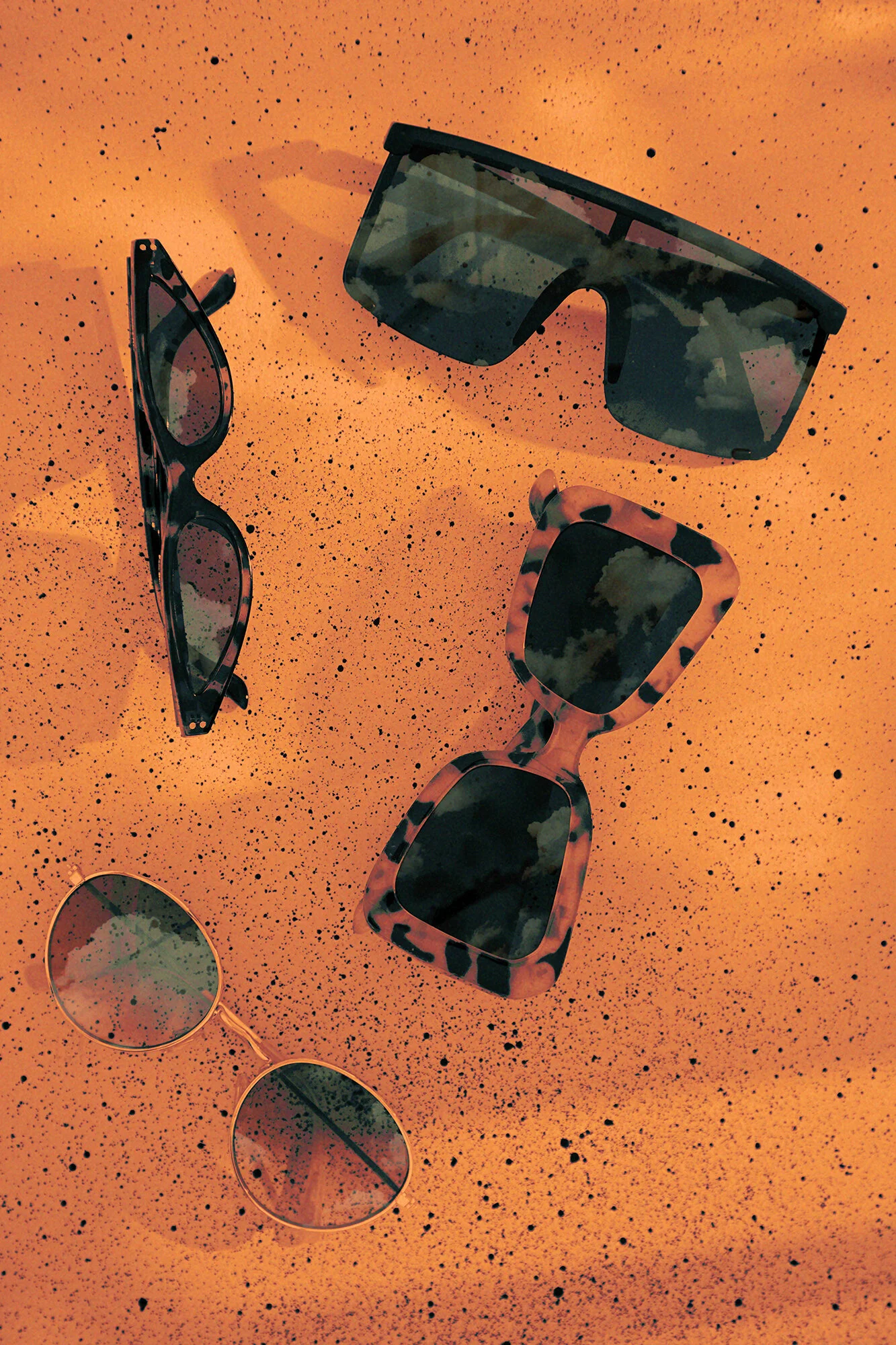 Several pairs of sunglasses with different frame styles and colors are scattered on an orange speckled surface.