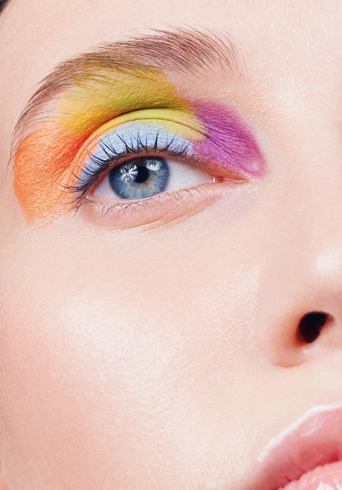Close-up of a person's eye with bright eyeshadow in shades of yellow, pink, blue, and orange around the eyelid.