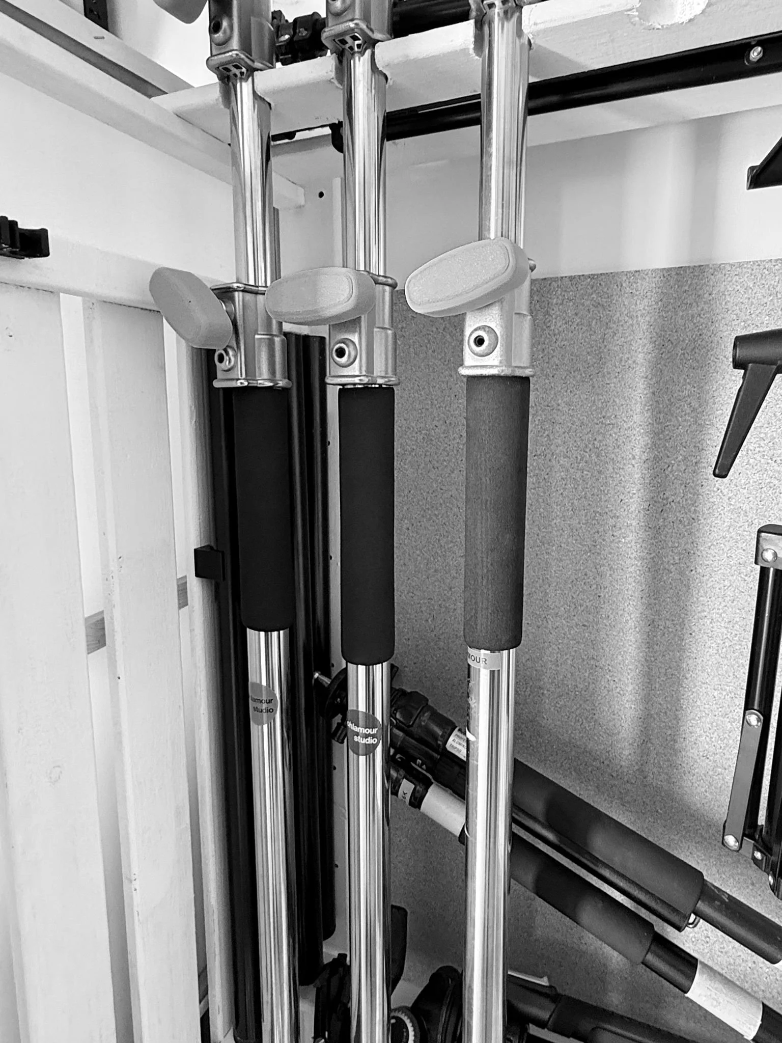 A set of parallel metal roller push carts with foam handles, positioned vertically against a wall and a shelf with various items underneath.
