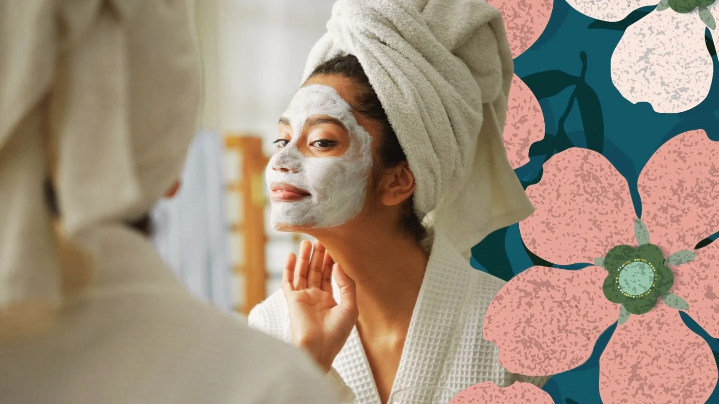 A woman with a towel wrapped around her head and a facial mask on her face, looking at herself in the mirror.