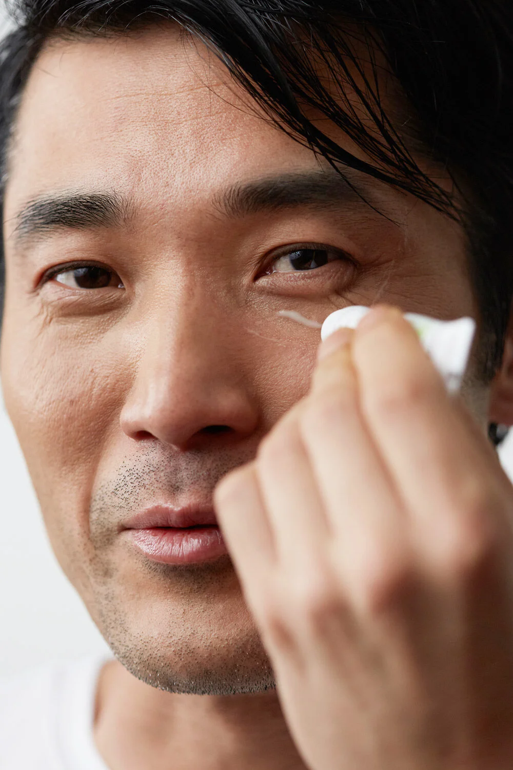 Close-up of a man applying eye cream or moisturizer under his right eye with his finger.