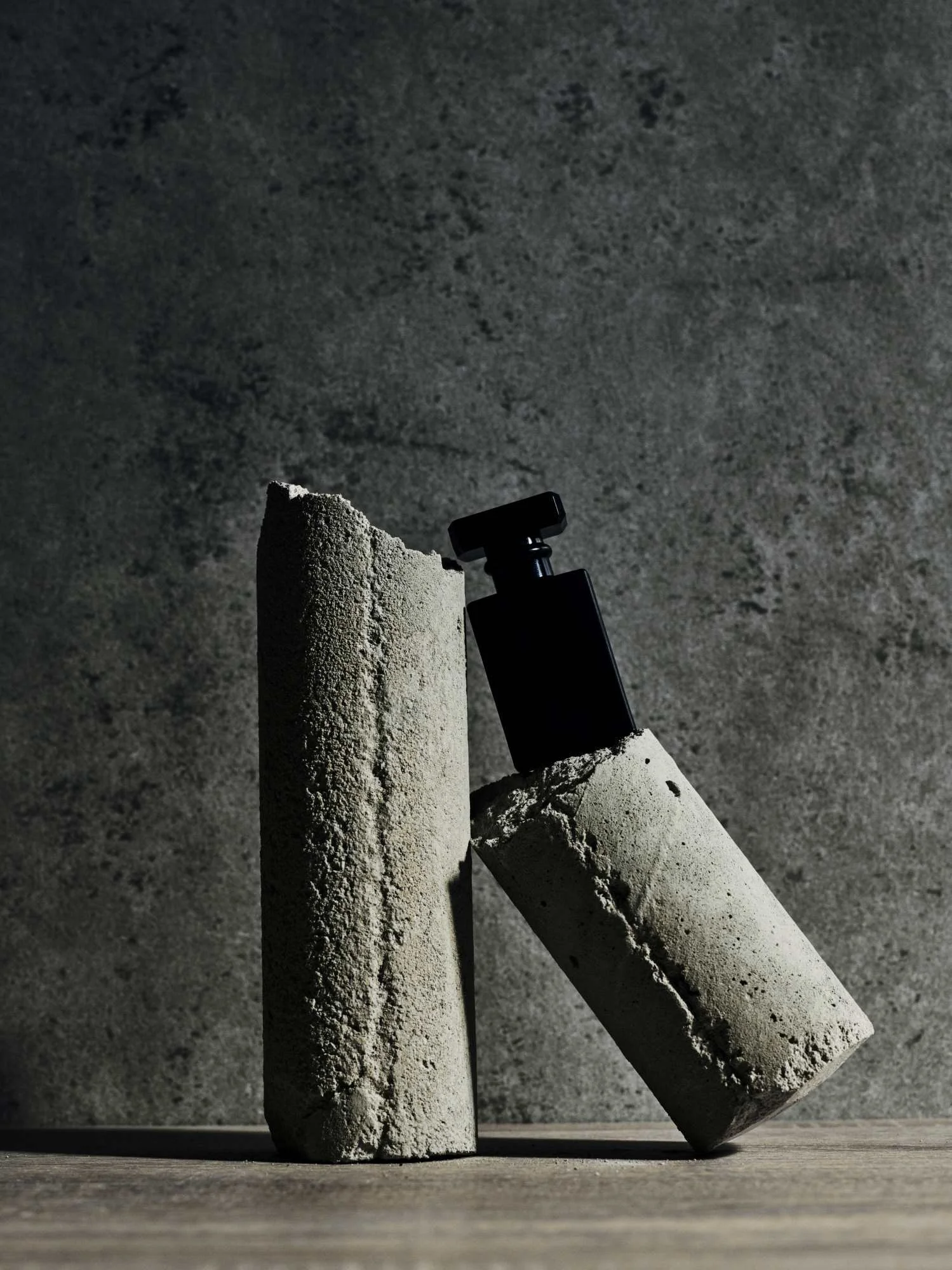Three pieces of chalk and a black chalk holder on a wooden surface with a rough gray wall in the background.