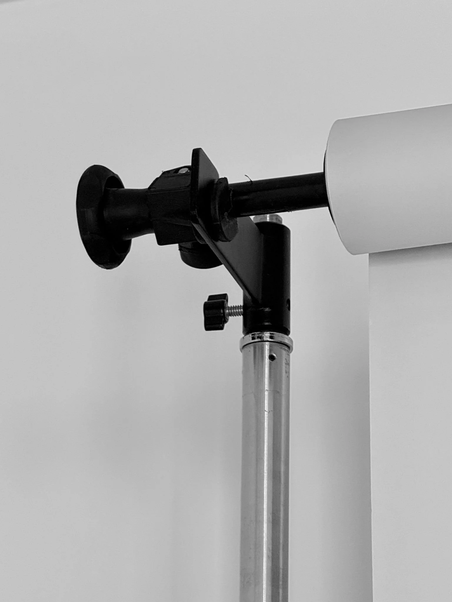 A zoomed-in view of a metal microscope stand with a white screen attached, set against a plain white wall.