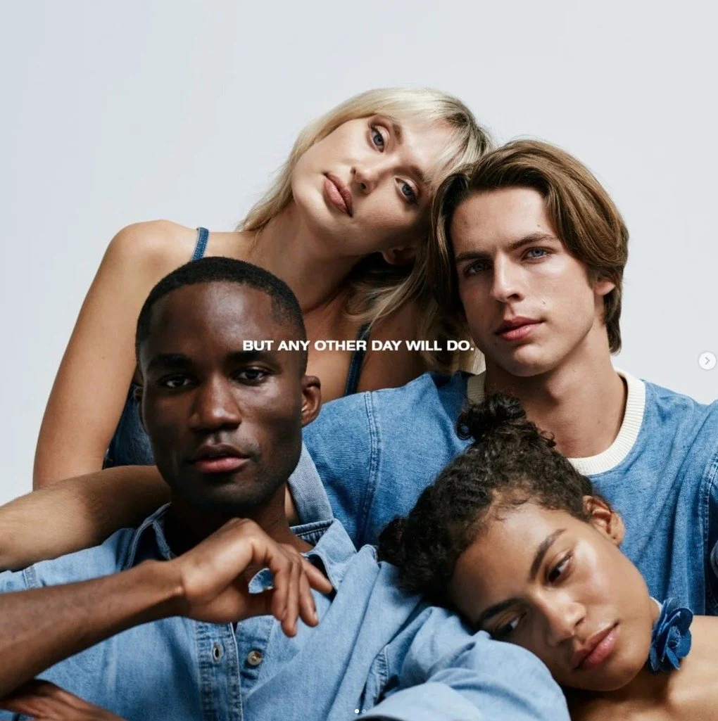 A diverse group of five young adults posing closely together against a white background, with one woman resting her head on another person's shoulder. The group appears relaxed and confident, with an overlaid text that says, 'BUT ANY OTHER DAY WILL D
