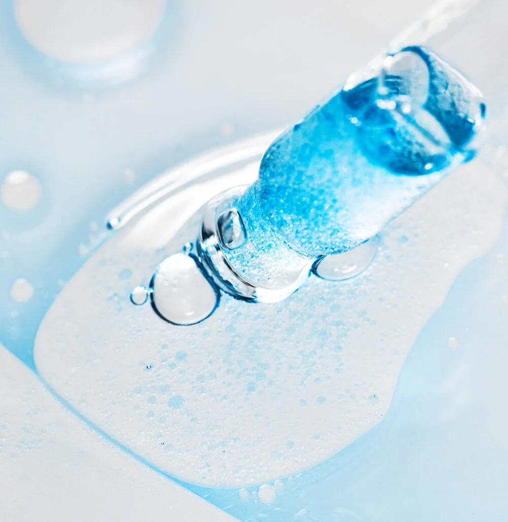 Close-up of a clear glass thermometer submerged in a liquid filled with ice, capturing melting ice and water droplets.