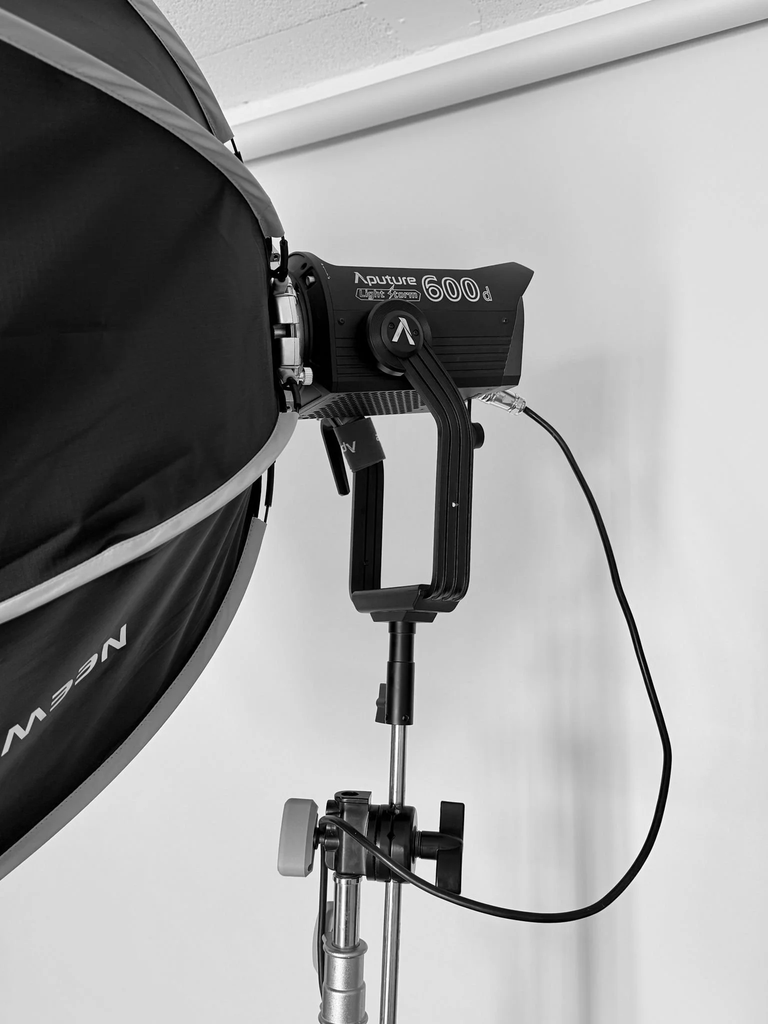 Close-up of a professional studio strobe light labeled "Aputure Light Storm 600d" mounted on a light stand, with part of a softbox or reflector visible on the left.