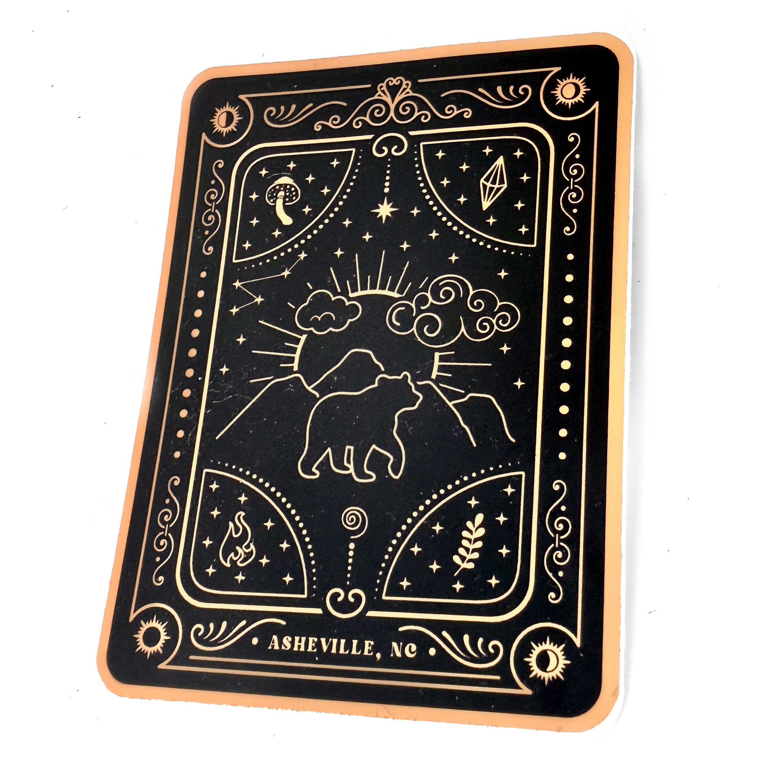 Close-up of a matte laminated sticker with celestial and nature motifs, reading Asheville, NC.