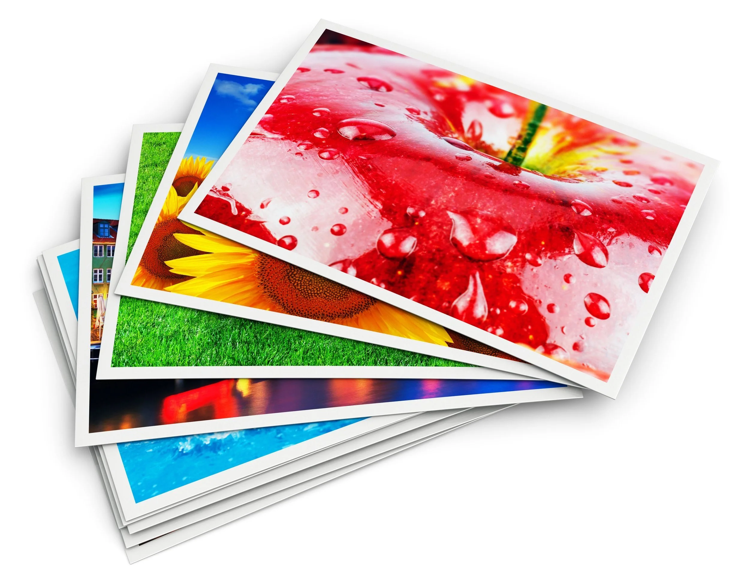 Stack of colorful printed photographs featuring nature scenes, including a close-up of a red flower with water droplets, a sunflower, a blue sky with clouds, green grass, a house, and a cityscape at sunset.