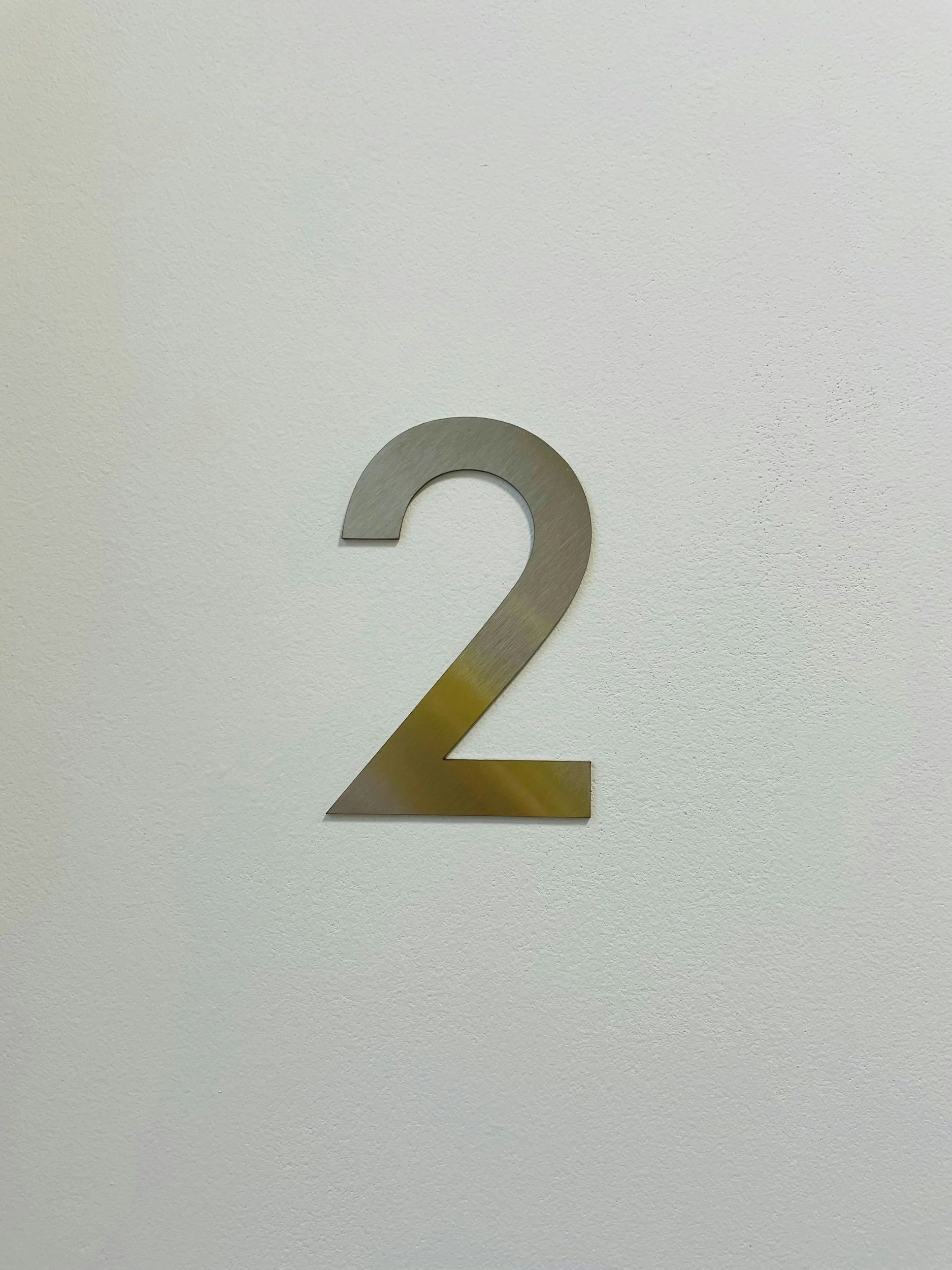 Close-up of a metallic number two on a plain white wall.