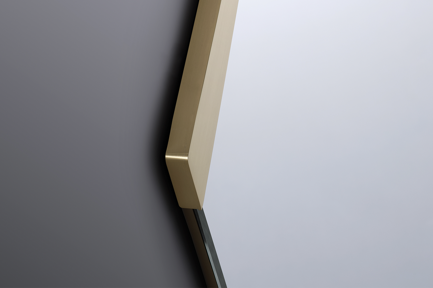 Close-up of the Strata Mirror showing the angled brass corner and subtle surface transitions.