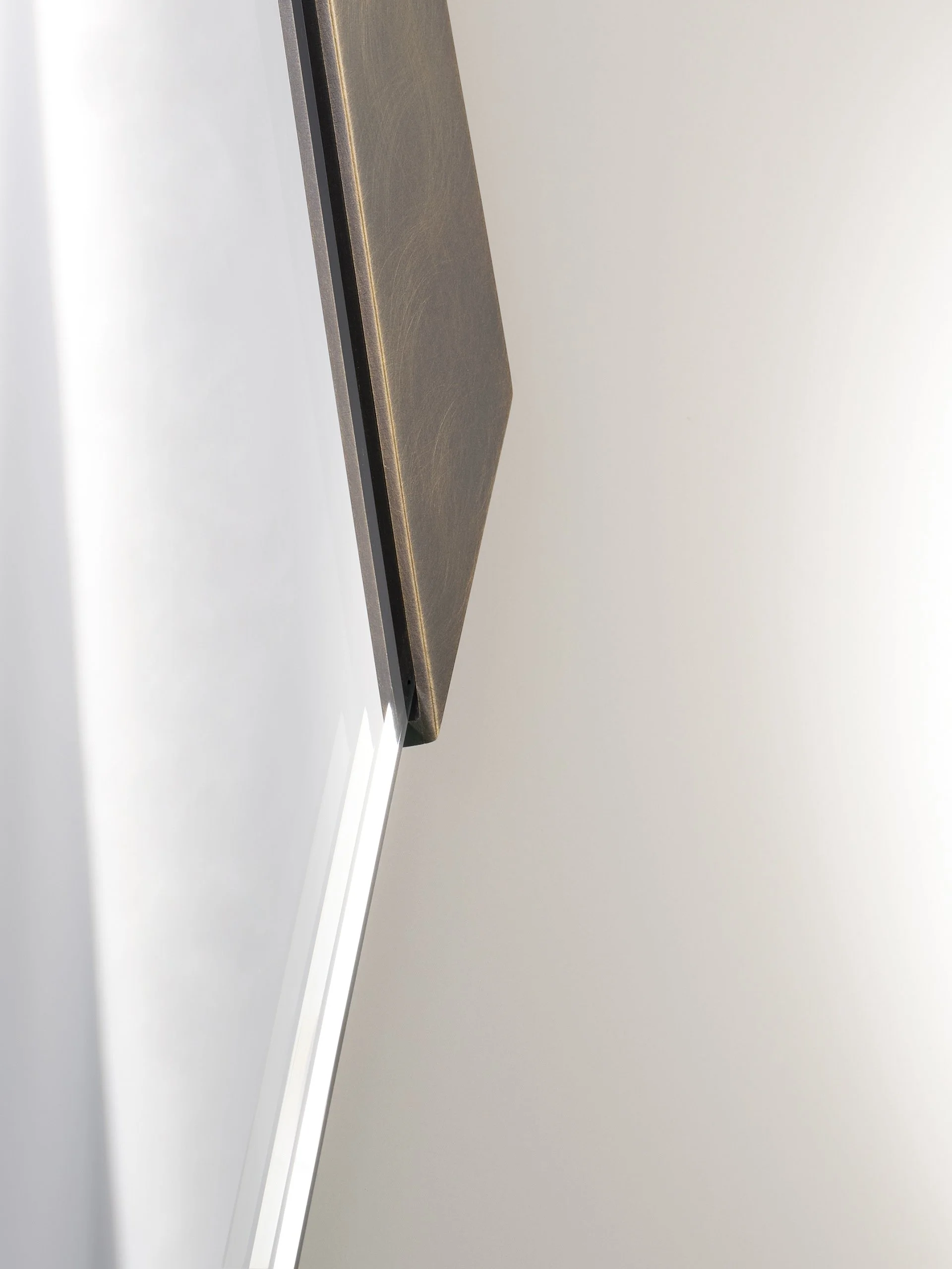Detail of the Strata Mirror’s sculpted brass edge and starphire-glass reflection with chamfer detail.