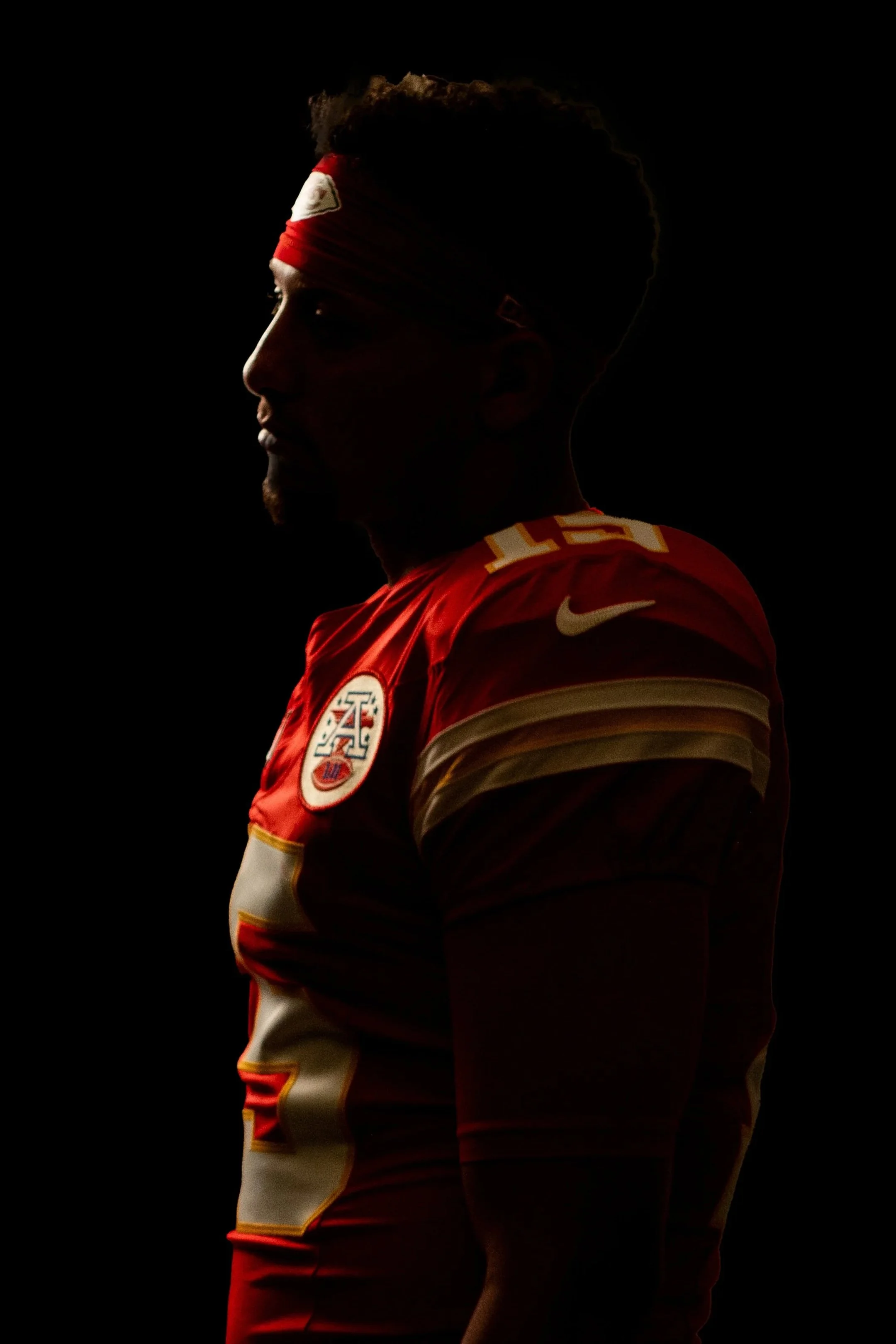A silhouette of a man in a red sports jersey with gold and white accents, standing against a dark background, with the Kansas City Chiefs logo and Nike swoosh visible.