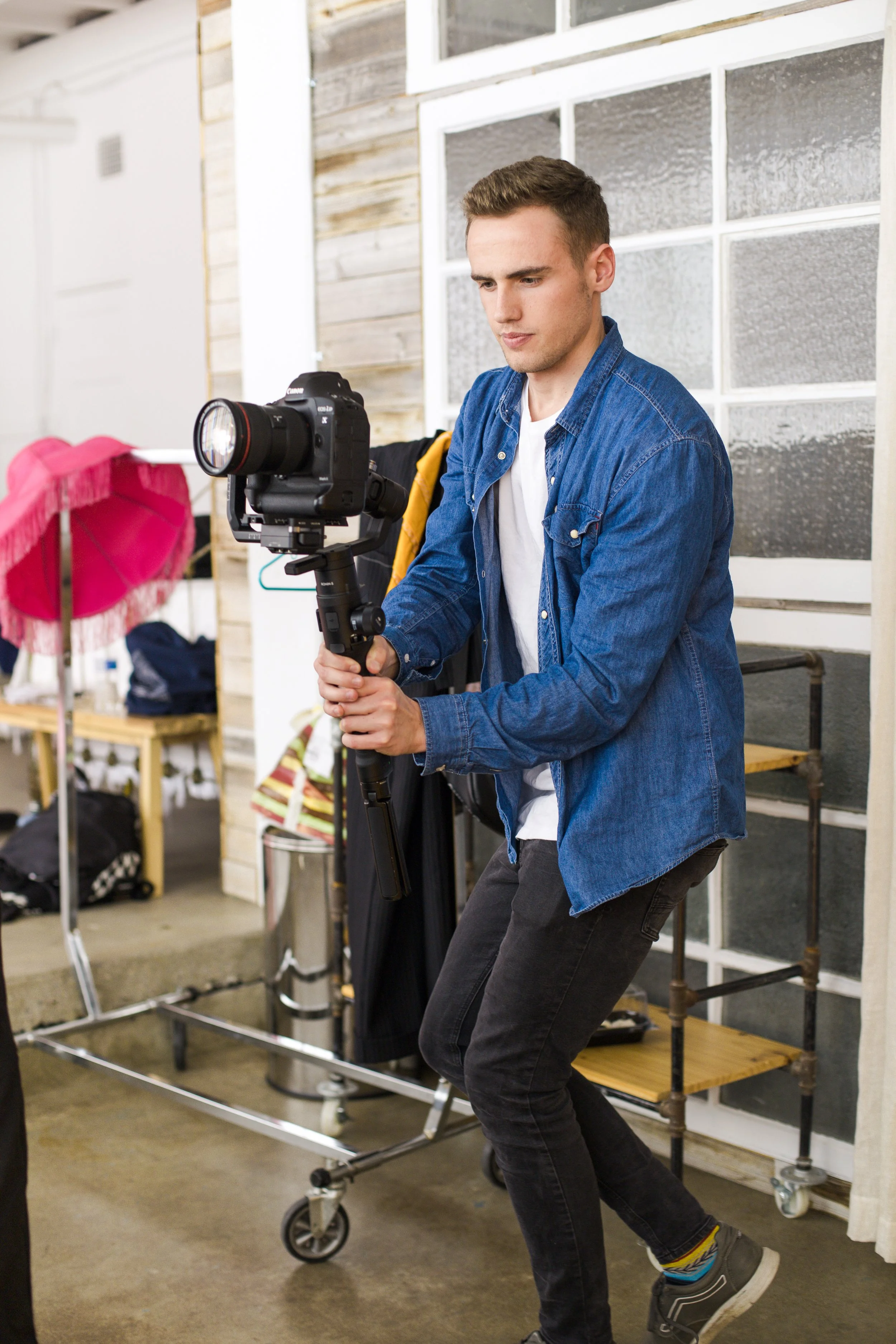 A man in a blue denim jacket holding a camera on a stabilizer in an indoor setting.