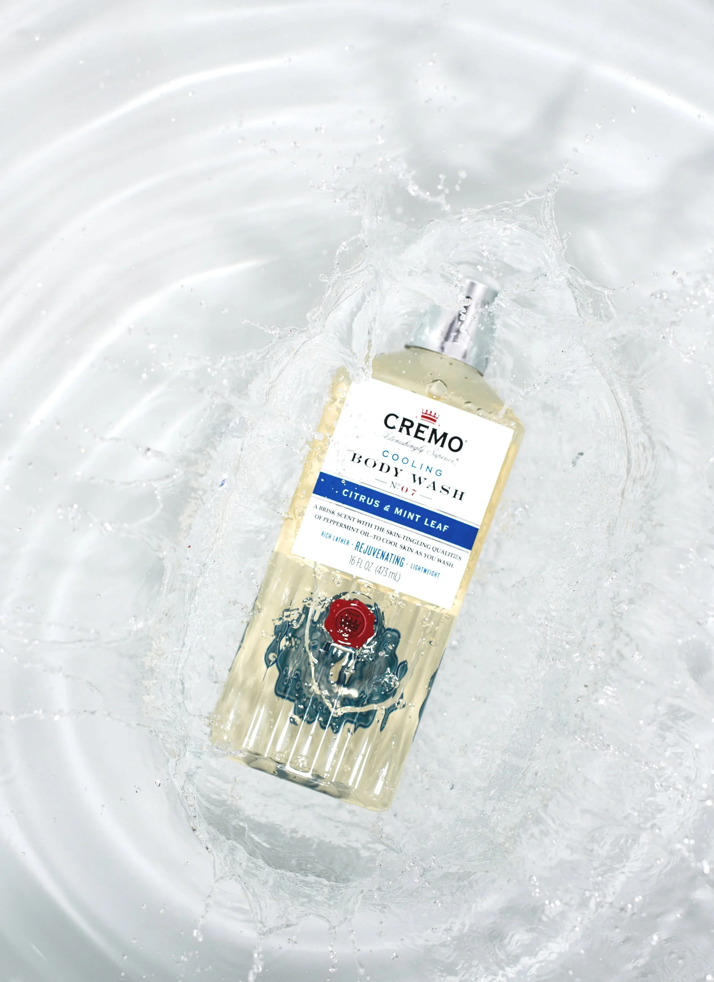 A bottle of Cremo cooling body wash with citrus and mint leaf scent floating in water.