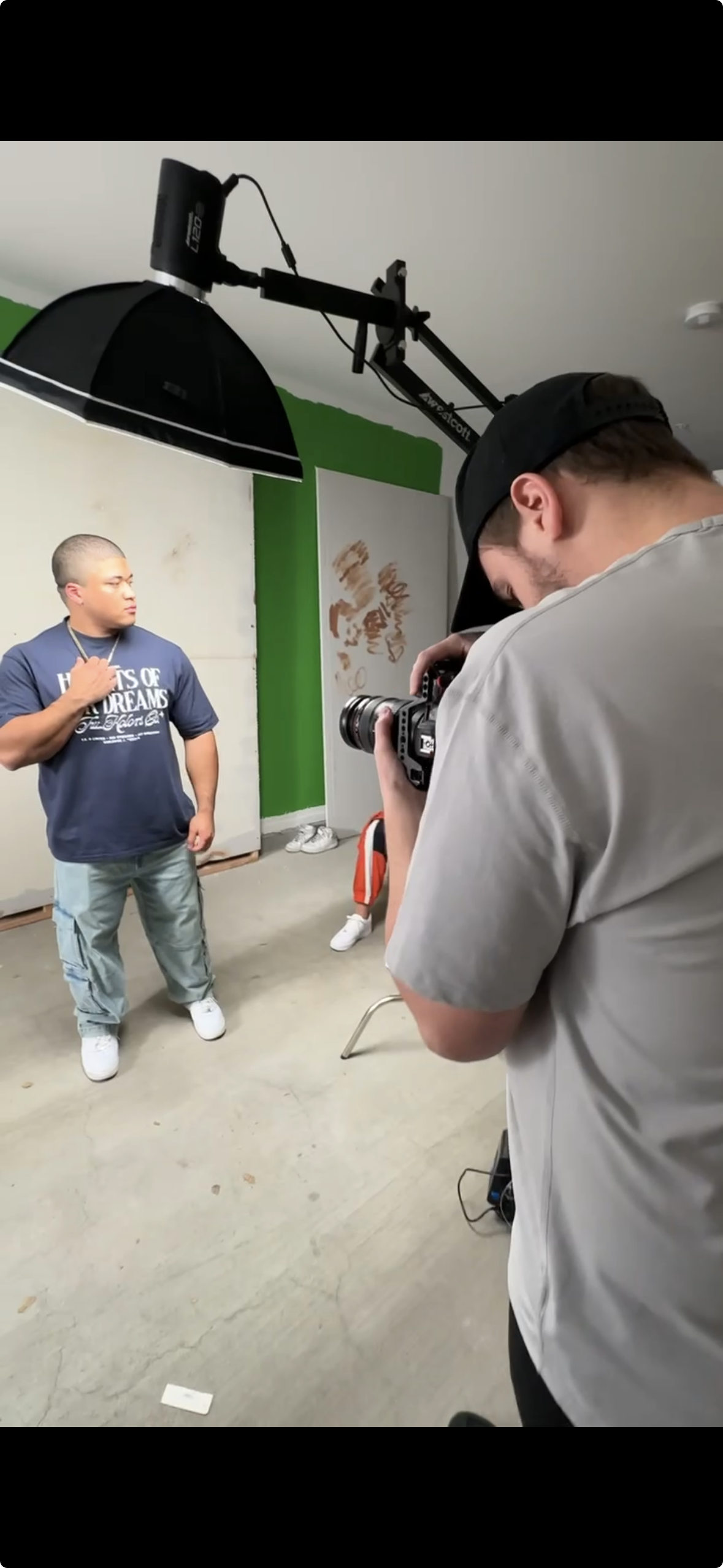Photographer taking a portrait of a man in a photography studio with a green and white backdrop and professional lighting equipment.