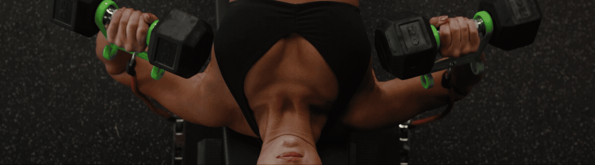 A person is lying on a workout bench doing a dumbbell chest press, with their arms extended holding black dumbbells with green accents.