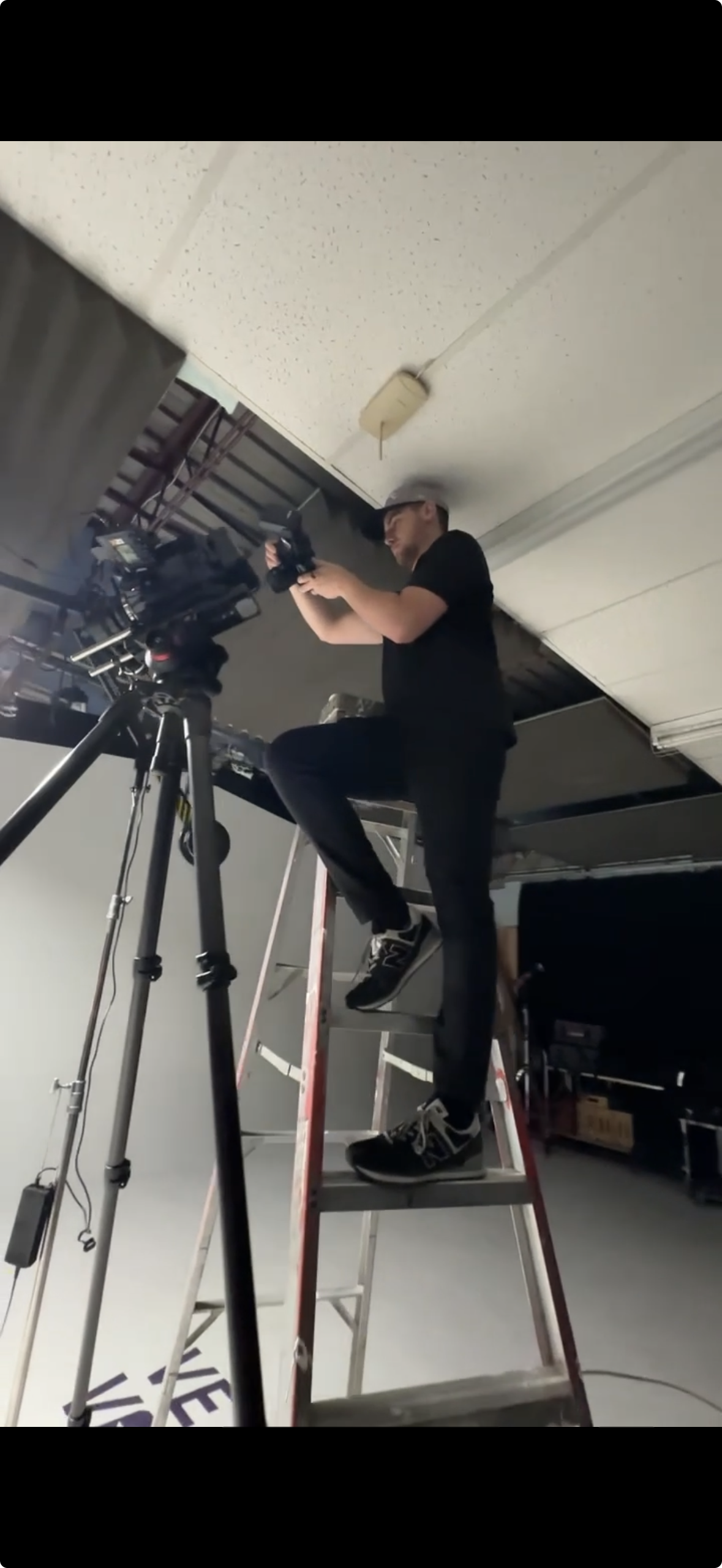 A person standing on a ladder, working with camera equipment in a studio setting.