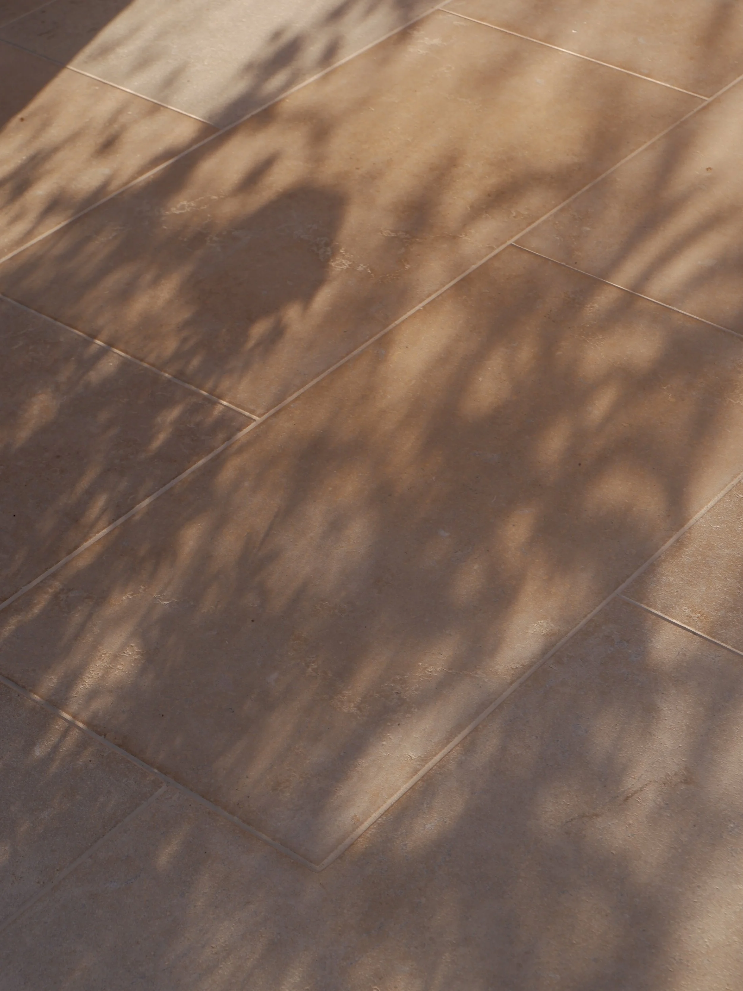 Close-up of brown ceramic tile flooring with shadow patterns. Harrington Brothers Landscapes Surrey.