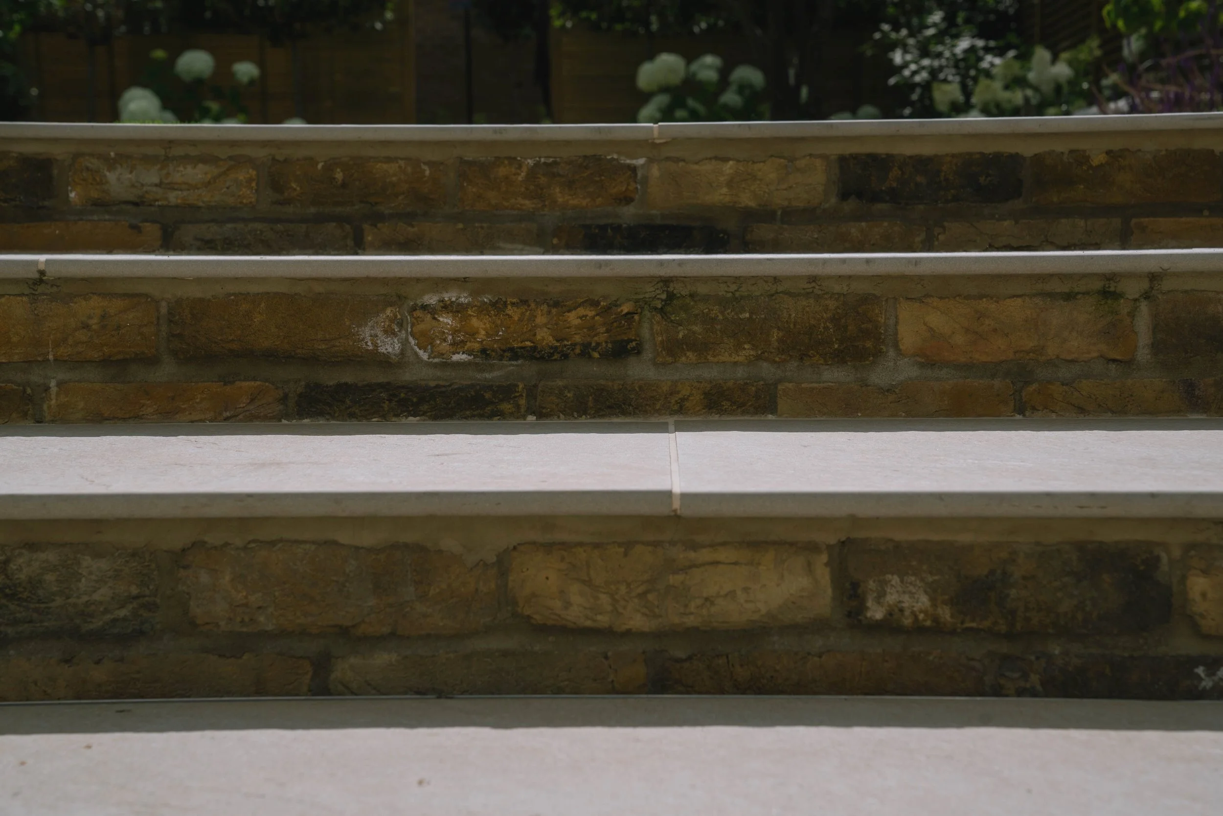 Close-up of brick stairs with white trim, outdoors with foliage in the background.