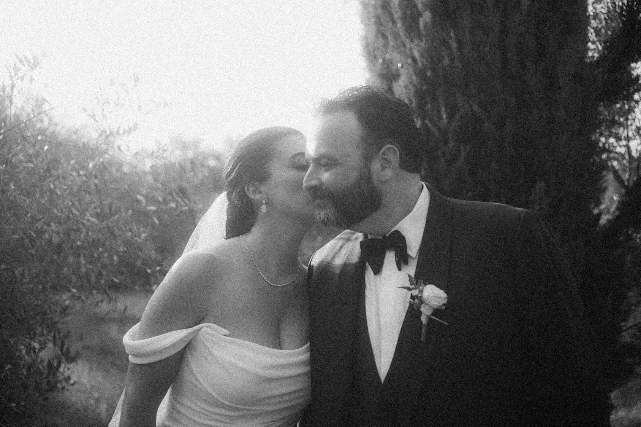A bride give a groom a kiss on the cheek amidst the rows of olive trees after their ceremony at a villa in Tuscany.
